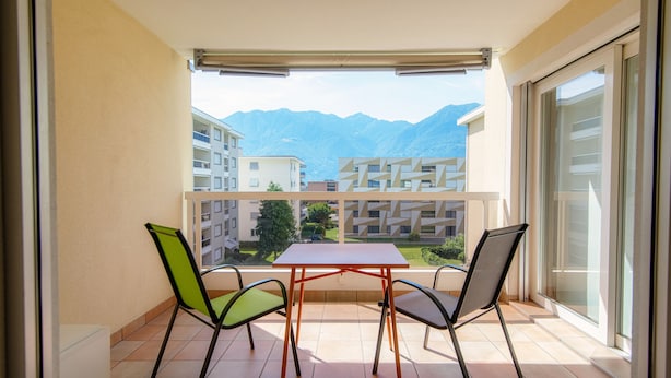 Un balcón con una mesa y dos sillas, con vistas a edificios y montañas.