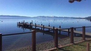 Un lago tranquilo con un muelle de madera que se adentra en el agua, rodeado de montañas al fondo.