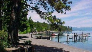 Un paseo junto al lago con un muelle que se adentra en el agua, rodeado de árboles y un cielo despejado.