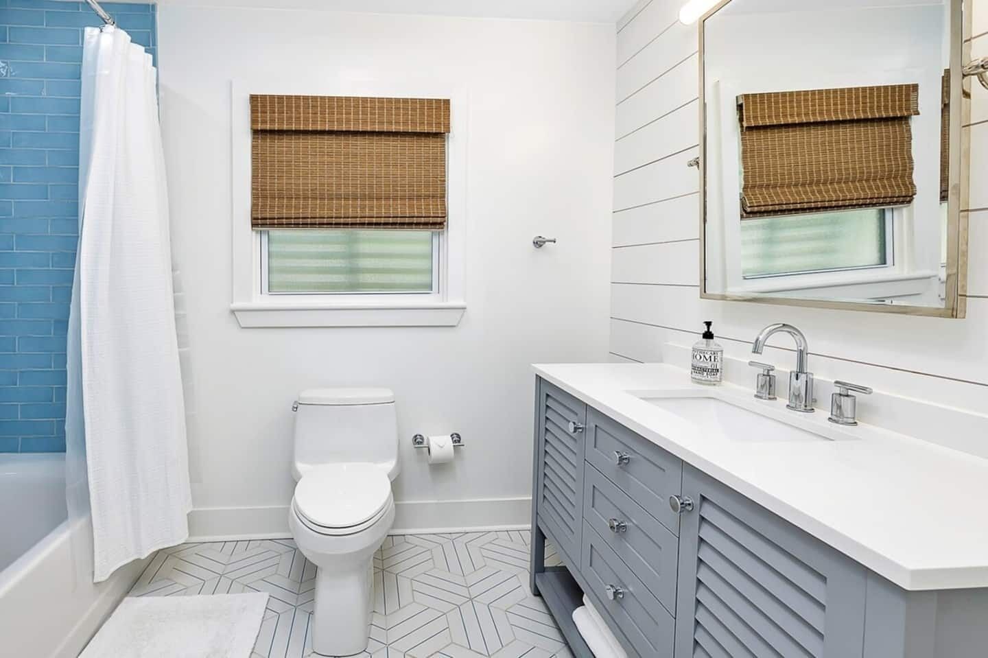A bathroom with a white toilet, a vanity with a mirror, and a window with a brown blind.