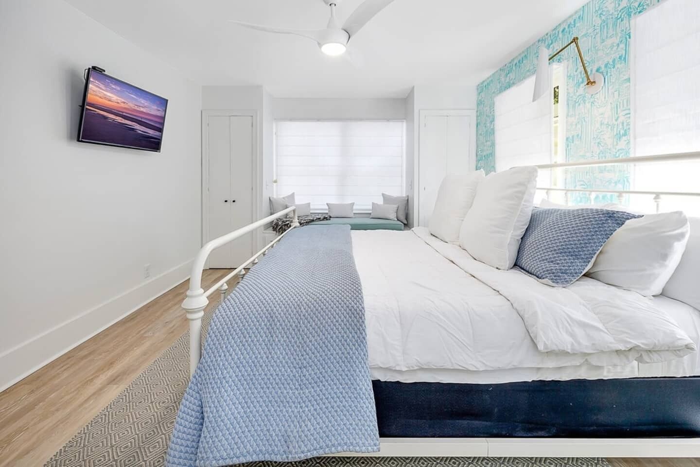 A bedroom with a bed, a window, a ceiling fan, and a wall-mounted TV.