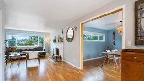 A spacious living room with hardwood flooring, a fireplace, a sofa, and a dining area with a table and chairs. - Perch - Gathering Spot: Spacious 5BR home in Shoreline (Shoreline)