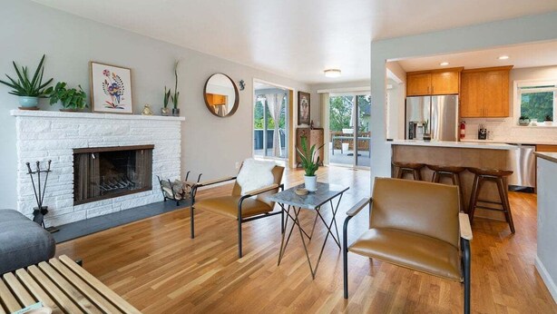 A modern living room with a fireplace, wooden flooring, and a dining area with a table and chairs. - Perch - Gathering Spot: Spacious 5BR home in Shoreline (Shoreline)