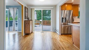 A modern kitchen with stainless steel appliances, a wooden dining area, and a sliding glass door leading to a deck. - Perch - Gathering Spot: Spacious 5BR home in Shoreline (Shoreline)
