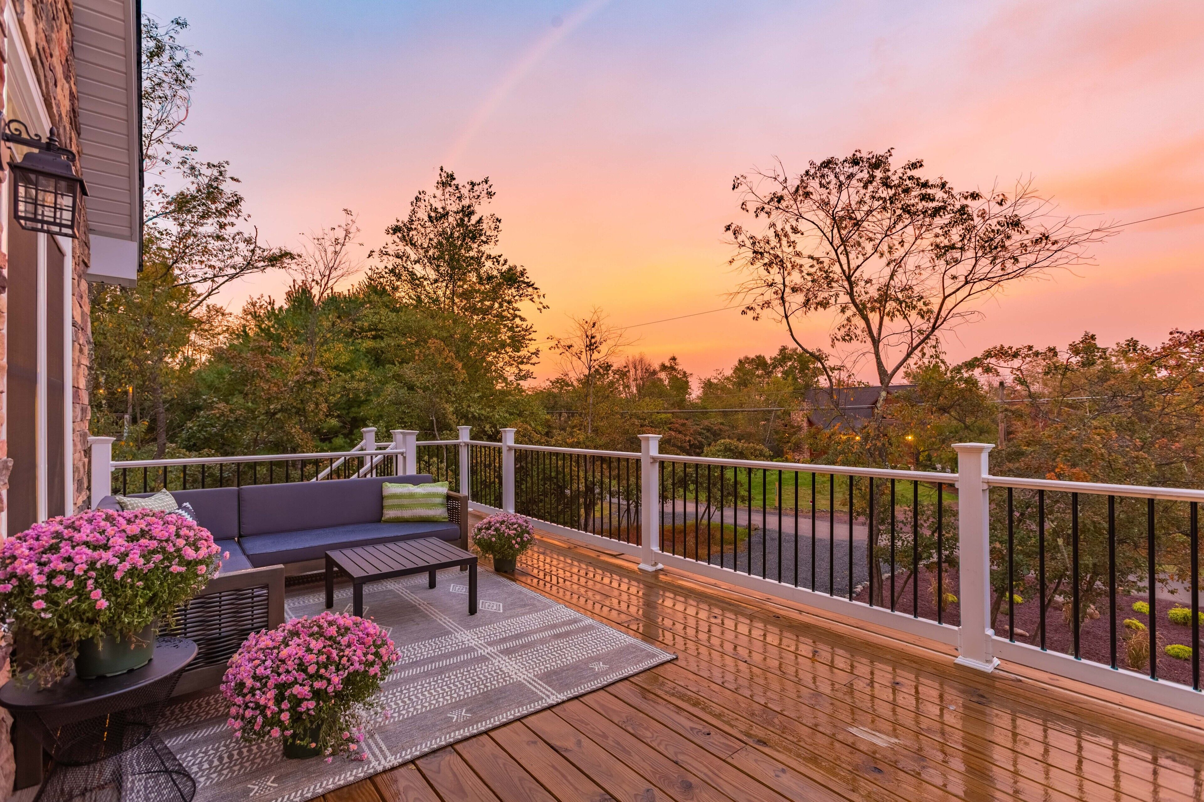A wooden deck with a white railing, a black outdoor sofa, and pink flowers.