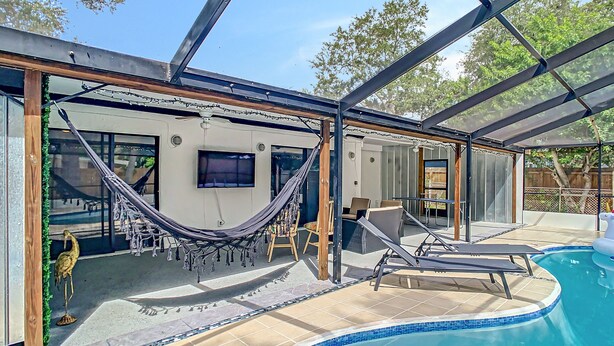 A covered outdoor area with a pool, a hammock, and a TV mounted on the wall.