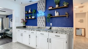 A modern kitchen with white cabinets, a marble countertop, and a neon sign on the wall.