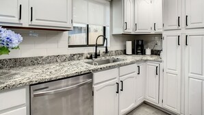 A modern kitchen with white cabinetry, a granite countertop, stainless steel appliances, and a window with a view.