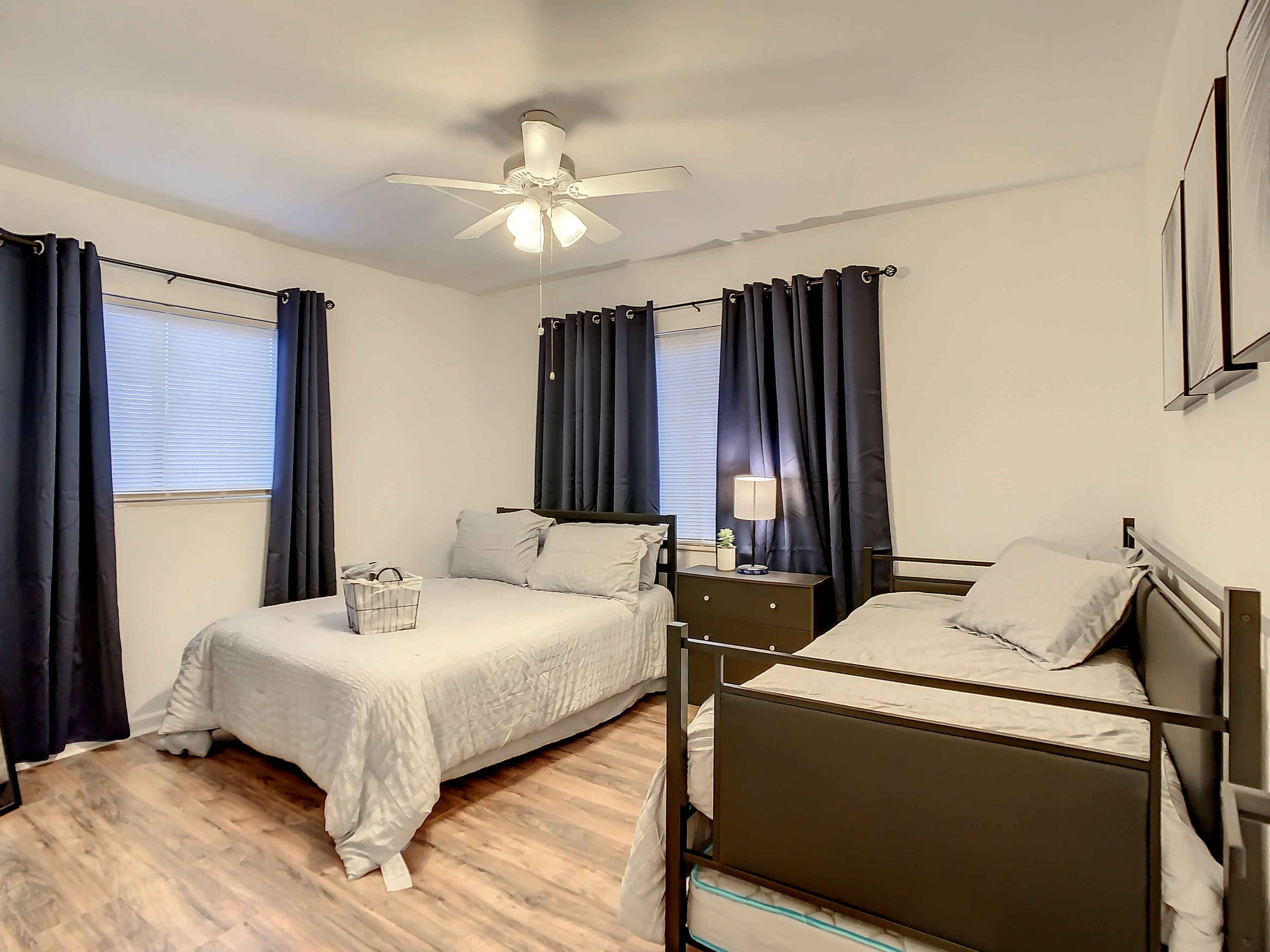 A bedroom with a single bed, a smaller bed, a nightstand, a lamp, and a ceiling fan.