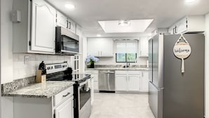 A modern kitchen with white cabinets, stainless steel appliances, and a 'Welcome' sign.