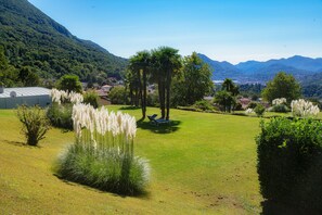 A lush green lawn with a gazebo, pampas grass, and a view of a town and mountains in the background. - Cadro Garden (Lugano)