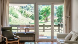 A room with a sliding glass door leading to an outdoor patio, a sofa, a chair, and a table. - Cadro Garden (Lugano)