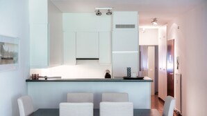 A modern kitchen with white cabinets, a glass island, and a dining area with a table and chairs. - Cadro Garden (Lugano)