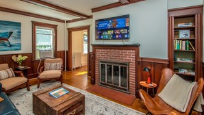 A living room with a fireplace, a television mounted on the wall, a bookshelf, and a painting on the wall. - Historic Wolfeboro Home one block to Village (Wolfeboro)