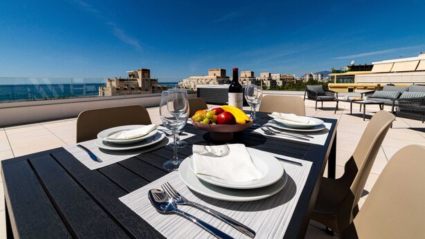 A table set for two with plates, cutlery, and a bowl of fruit, overlooking a coastal cityscape. - PREMIUM Apartment with 3 bedrooms. Capacity for 6 people (Marbella)