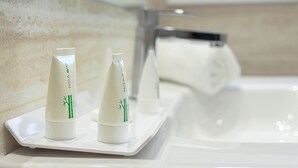 Dos botellas blancas con detalles de bambú verde sobre una bandeja blanca en un baño con un lavamanos y un espejo blancos.