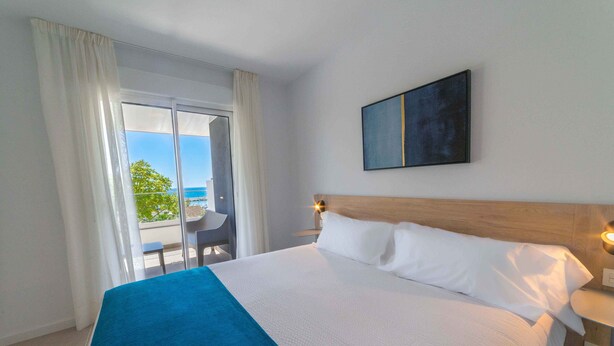 Habitación de hotel con una cama grande, vistas al mar a través de un ventanal corredero y un cuadro en la pared.