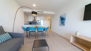 A modern living room with a grey sofa, a black coffee table, and a dining area with blue chairs and a white table. - Deluxe 2 Bedroom Apartment. Capacity for 4 people (Marbella)