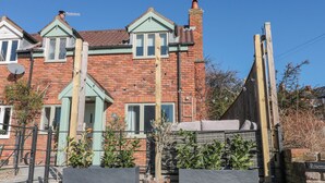 A two-story brick house with a green door and windows, a satellite dish, and a wooden fence.