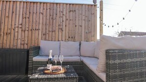 A wicker sofa with cushions, a small table with a bottle of champagne, two glasses, and a tray of snacks.