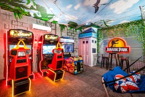 A room with two arcade machines, a plush toy in a hammock, and a 'Jurassic Park' themed wall.