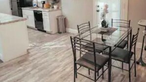 Une cuisine moderne avec des meubles blancs, un réfrigérateur noir et un coin repas comprenant une table en verre et des chaises en métal.