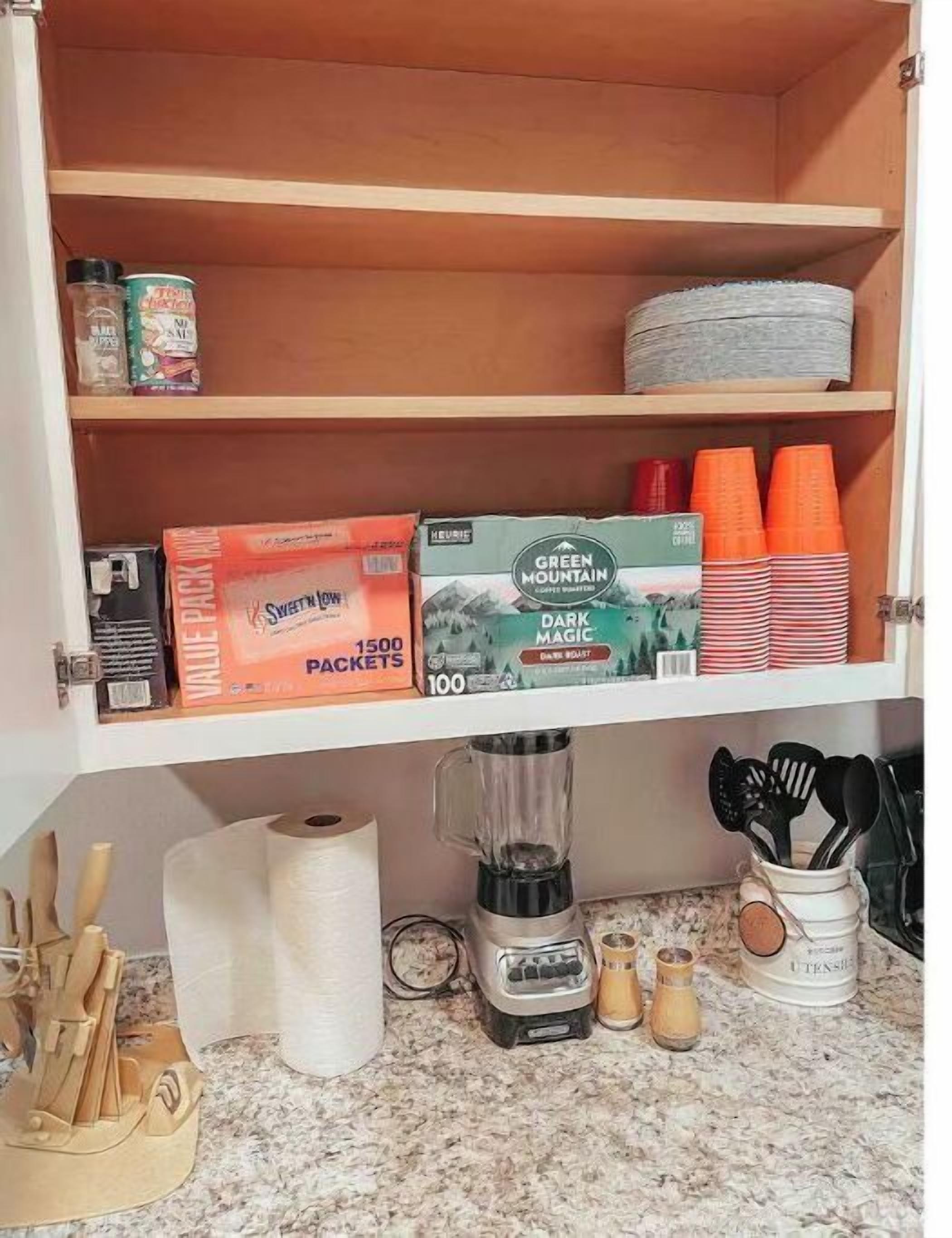 A kitchen with a wooden cabinet containing various items like a blender, cups, and kitchen utensils.