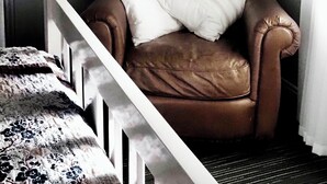 Une chambre d’angle avec un fauteuil en cuir marron, un berceau blanc et un mur orné de photos encadrées.