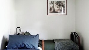 Une chambre à coucher avec un lit, une table de chevet avec une lampe, un tableau encadré au mur et un radiateur.