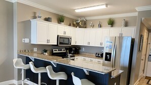 Eine moderne Küche mit weißen Schränken, einer zentralen Kochinsel mit Barhocker, einem Kühlschrank und einer Mikrowelle.