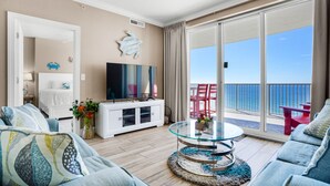 Ein geräumiges Wohnzimmer mit einem großen Glastisch, einer weißen Unterhaltungseinheit und Blick auf den Ozean durch große Schiebetüren.