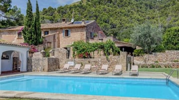 A pool area with lounge chairs and a stone building with a rustic design.