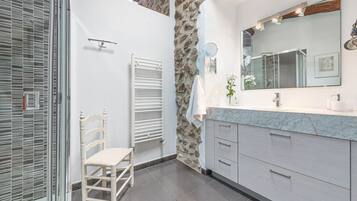A bathroom with a stone wall, a white chair, a large mirror, and modern cabinetry.