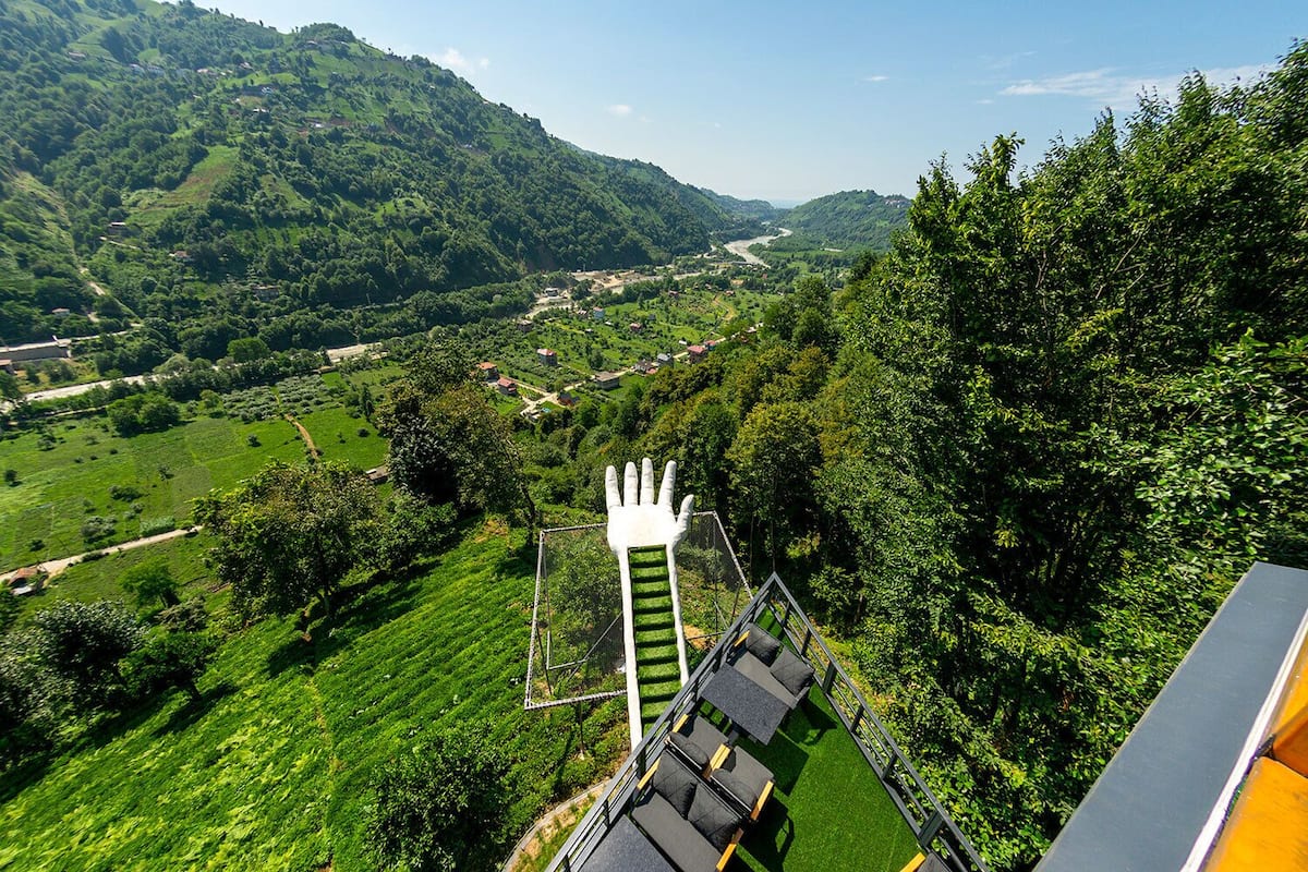 A scenic view of a valley with a large white hand sculpture in the foreground.