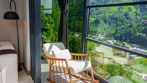 A room with a large window offering a view of a green landscape, a wooden rocking chair, and a floor lamp.