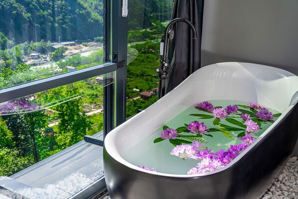 A bathtub with a view of a green landscape through a window.