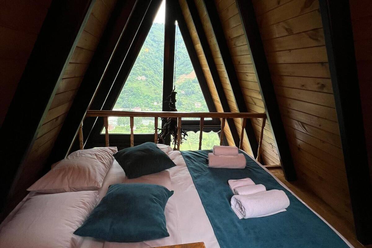 A bedroom with a wooden bed, pillows, and a view of a green landscape through a window.