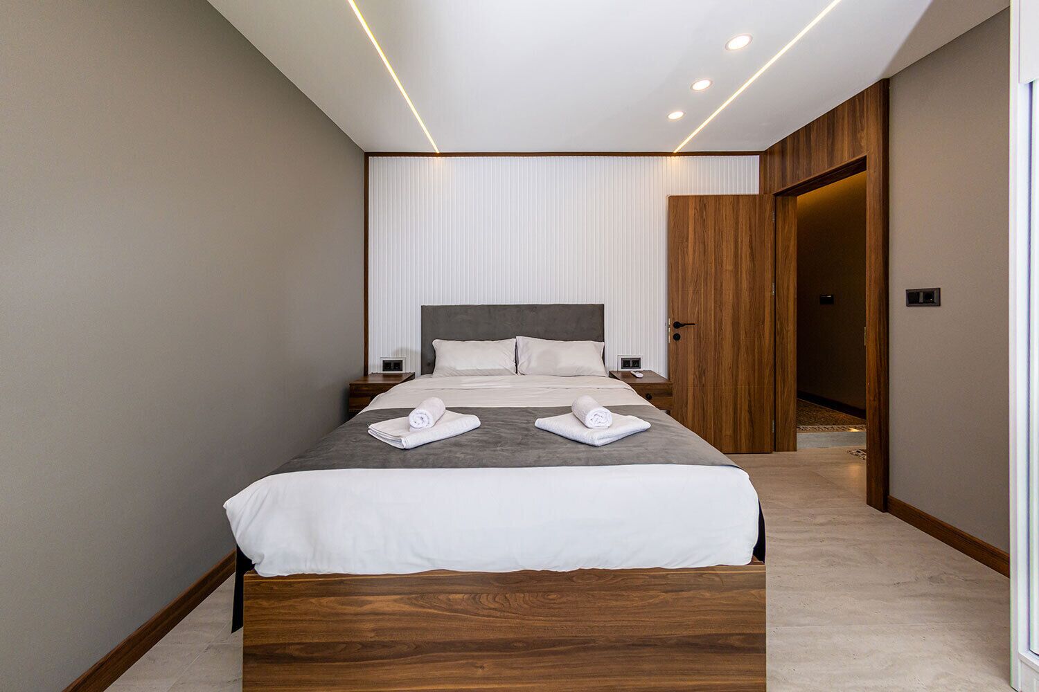 Una habitación de hotel moderna con una cama grande, cabecera de madera y una paleta de colores neutros.