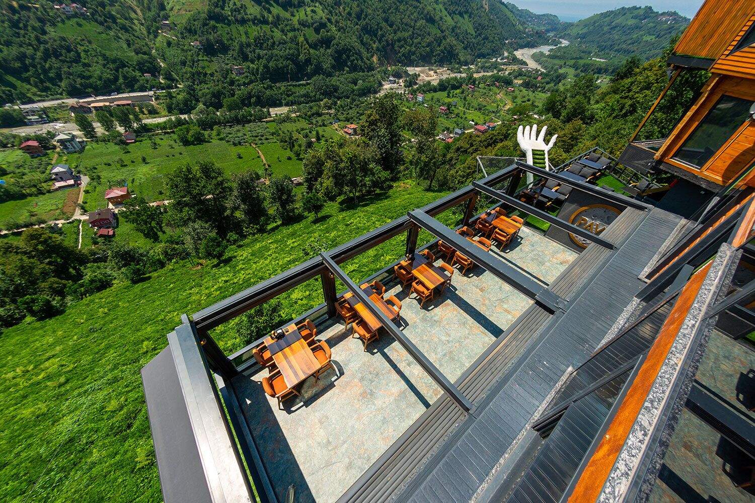 A modern building with a rooftop terrace featuring outdoor seating and a scenic view of a valley.