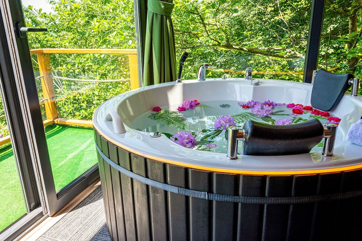 A hot tub with a glass top, surrounded by greenery, and a wooden deck.