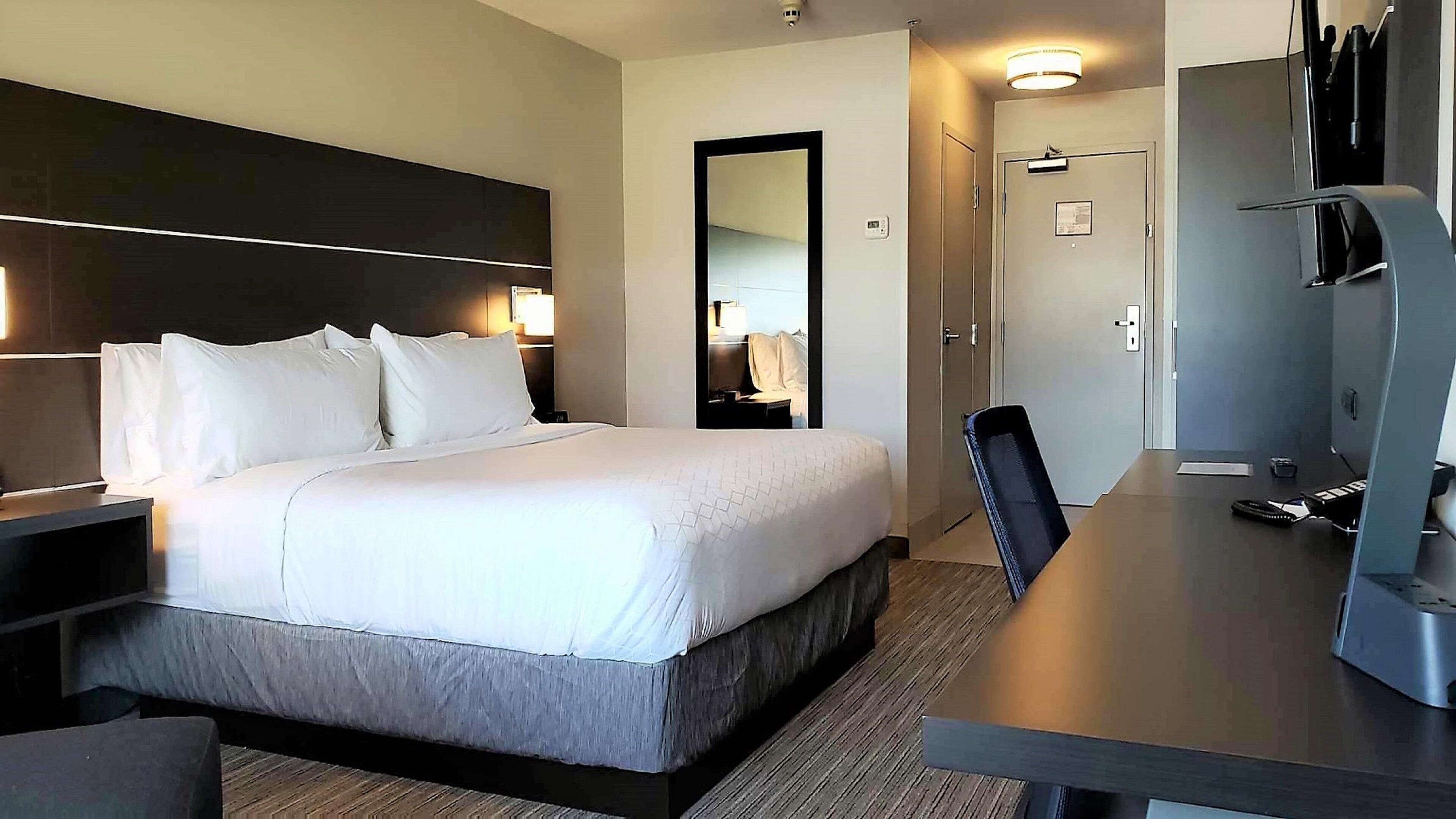 A hotel room with a large bed, a desk, a chair, a TV, and a mirror.