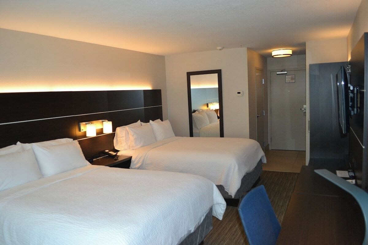 A hotel room with two beds, a desk, a mirror, and a refrigerator.