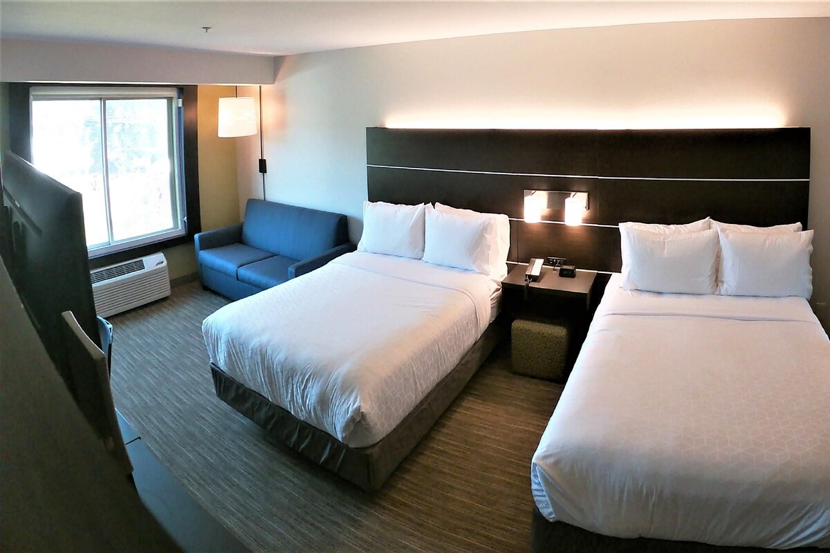 A hotel room with two beds, a sofa, a nightstand, a lamp, and a large mirror.