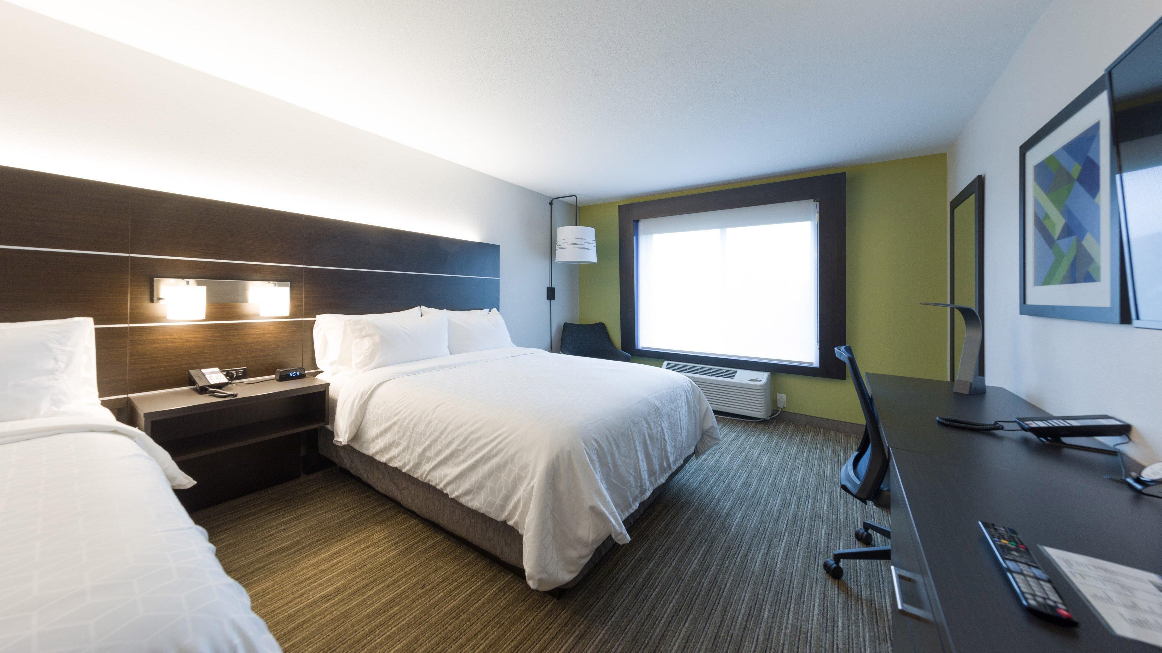 A hotel room with two beds, a desk with a computer, a phone, and a window with blinds.