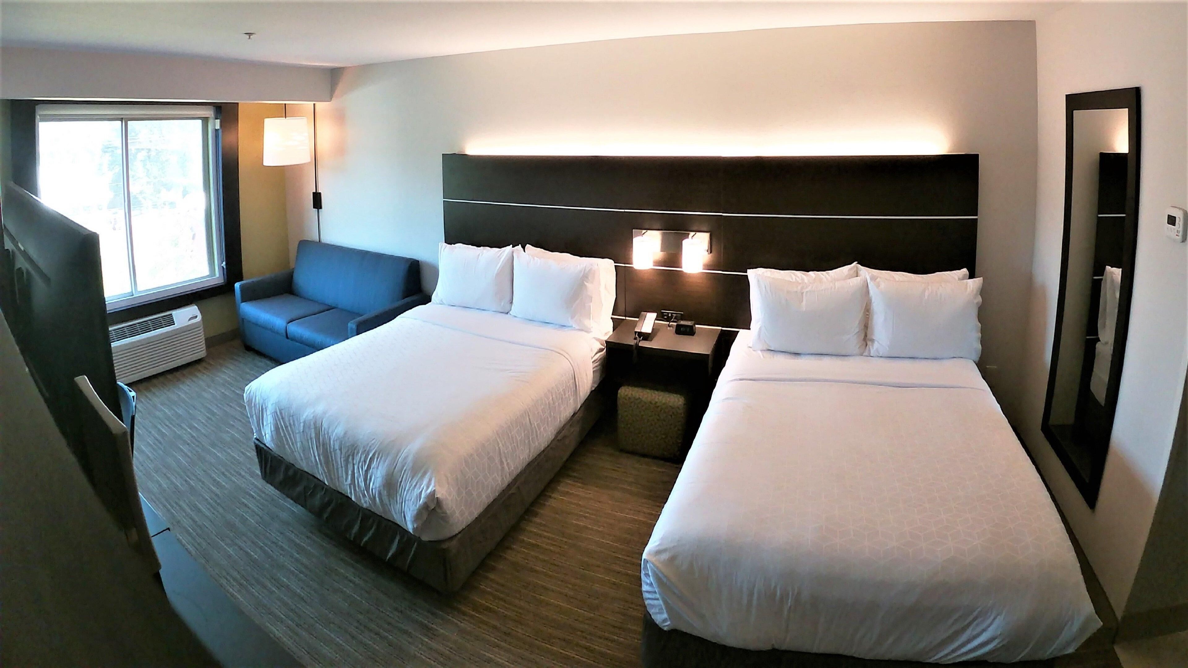 A hotel room with two beds, a sofa, a nightstand, a lamp, and a large mirror.