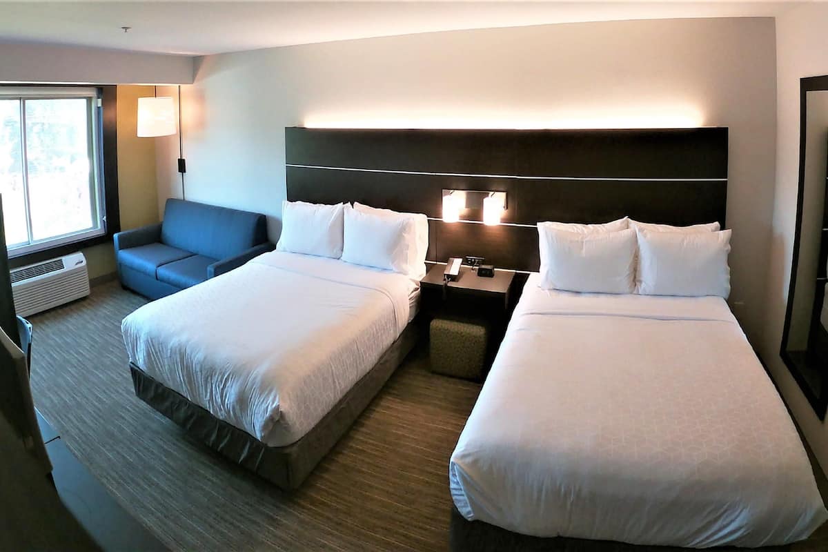 A hotel room with two beds, a sofa, a nightstand, a lamp, and a large mirror.
