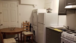 A compact kitchen with a dining area, including a wooden table, chairs, a washing machine, a refrigerator, a stove, and a sink. - Le Rameau RC (Montréal)