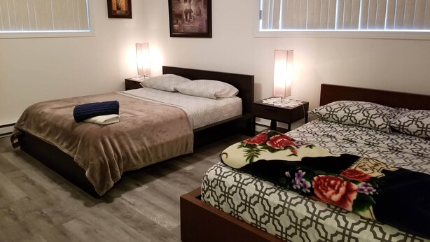 A hotel room with two beds, a nightstand with lamps, and artwork on the walls. - Le Rameau RC (Montréal)