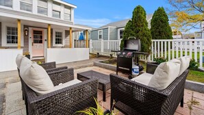 Un patio con mobiliario de mimbre, una parrilla y una cerca blanca.