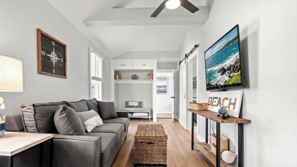 Una sala de estar moderna con un sofá gris, una mesa de centro de madera y un televisor montado en la pared.